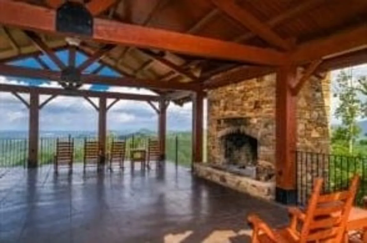 A spacious stone patio with rustic wooden rocking chairs, centered around an outdoor stone fireplace. The scene opens to a wide view of the mountains, inviting guests to gather, relax, or enjoy fireside chats under the open sky.
