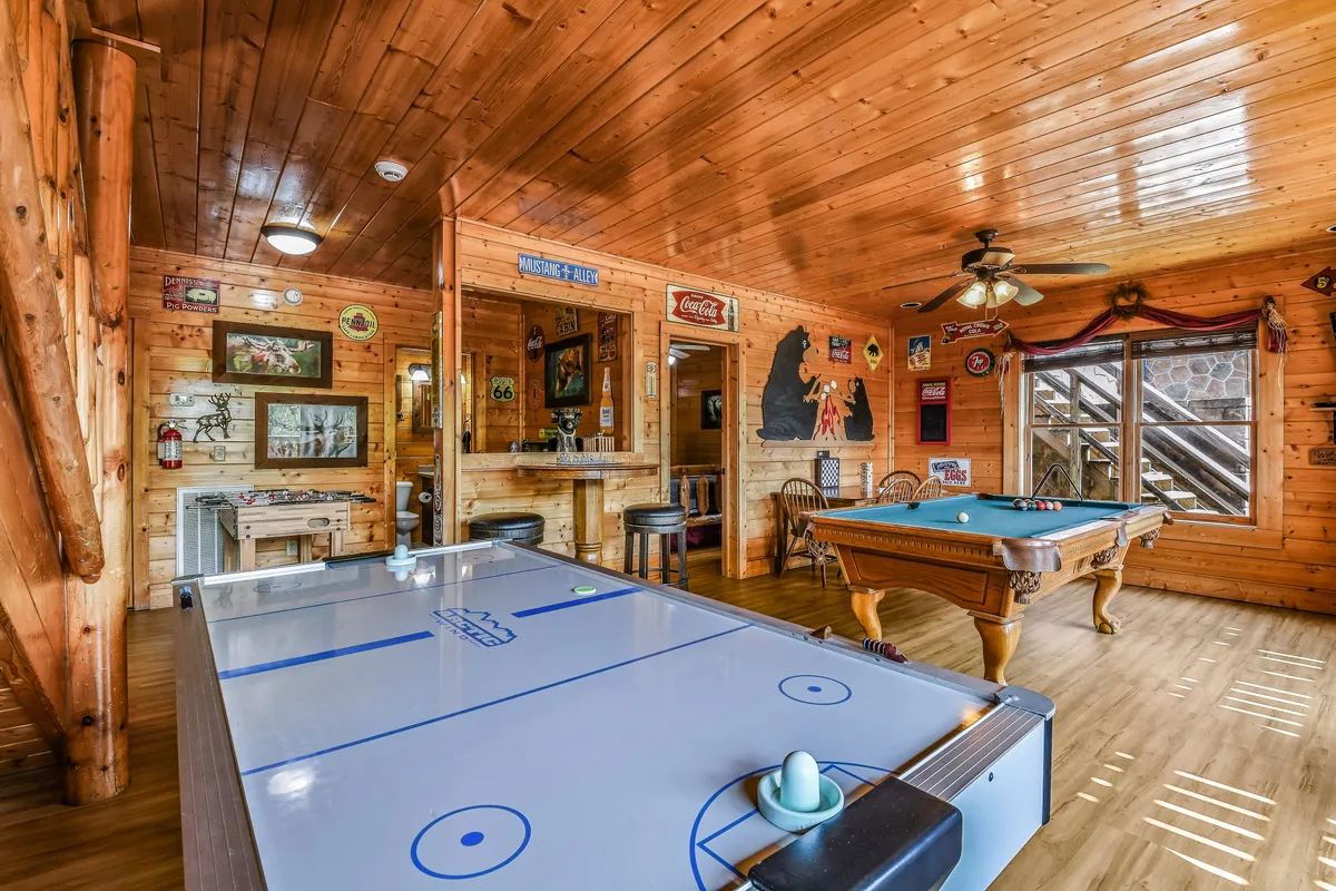 This interior image features a lively game room with both an air hockey and a pool table, a bar area for snacks and drinks, and decorative wall art that adds to the fun atmosphere. The space is clearly designed for entertainment and socializing, with ample room for friendly competition and group gatherings.