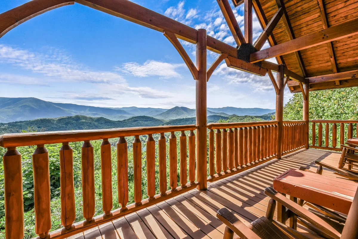 An inviting deck framed by wooden railings, overlooking expansive mountain views. Deck chairs are positioned for guests to relax and take in the peaceful scenery. The serene setting is bathed in natural light, suggesting a perfect spot for morning coffee, sunset-watching, or quiet conversations.