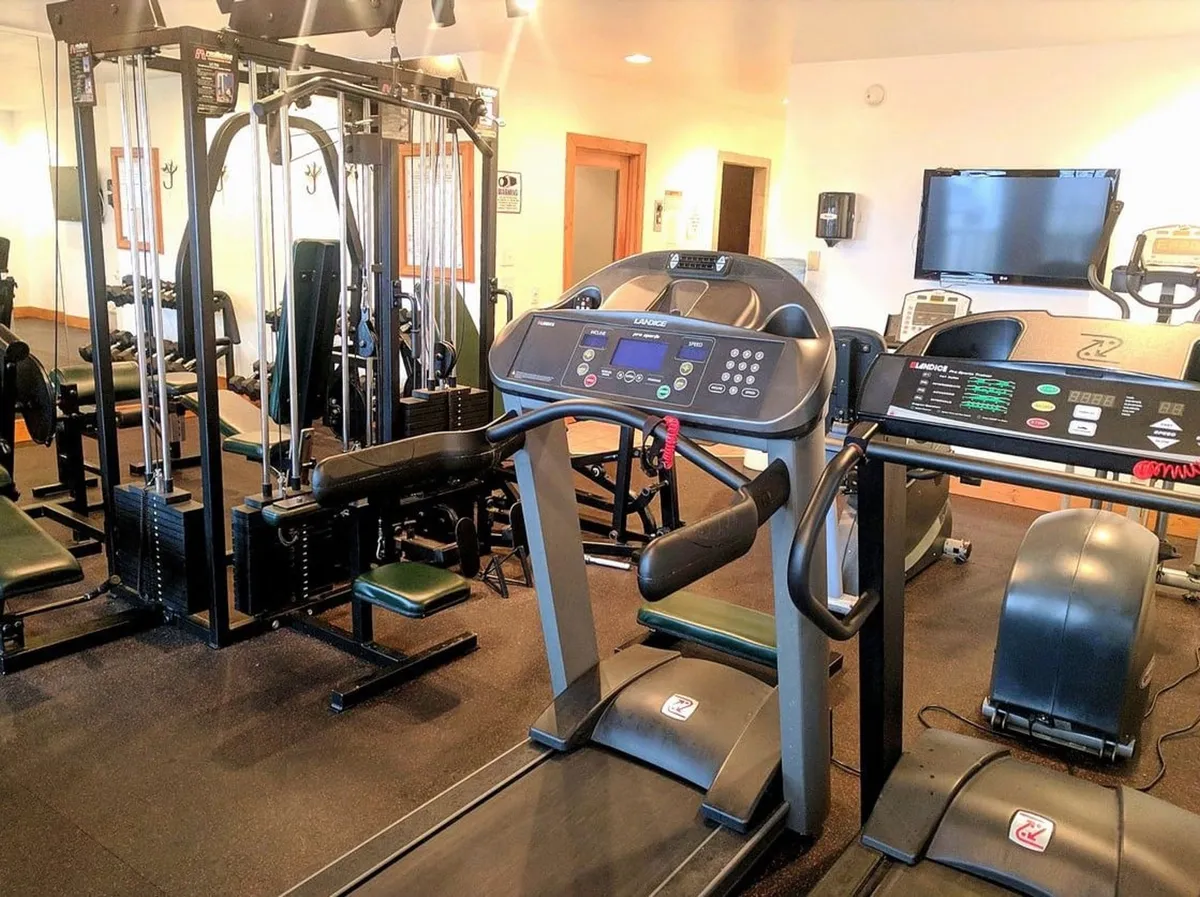 This interior shot features a modern, well-equipped gym with treadmills, weight machines, and exercise mats. The space is bright and airy, ideal for keeping up with fitness routines even while on vacation. A monitor and large windows make the setting feel welcoming and energizing.