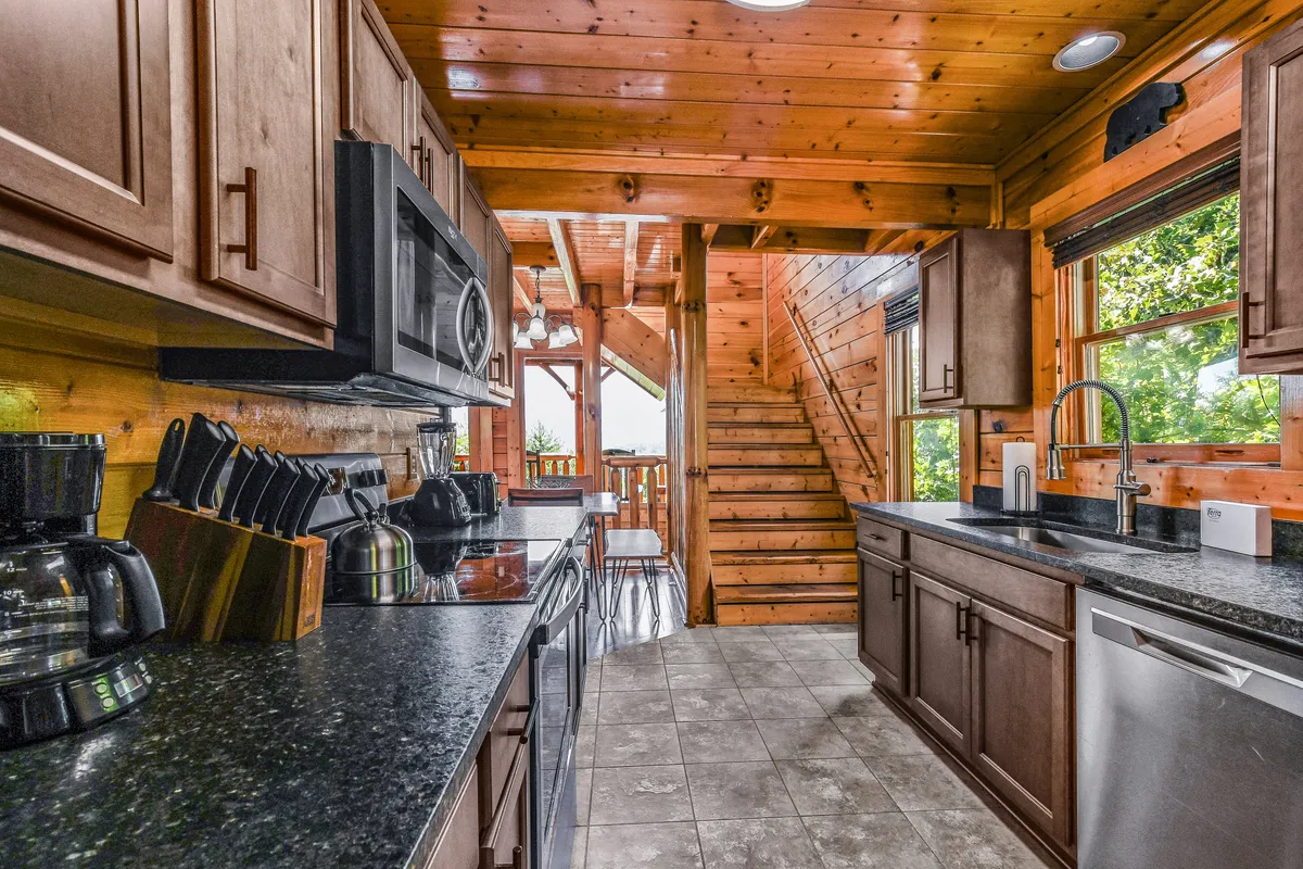 A stylish kitchen boasting granite countertops, modern stainless steel appliances, a wooden staircase, and large windows that let in natural light, making this an inviting hub for both casual breakfasts and festive gatherings.