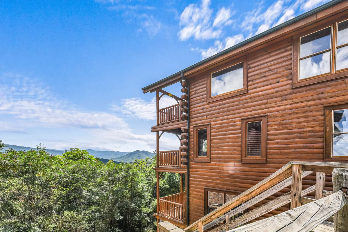 A wide view of a log cabin structure perched with balconies overlooking a stunning mountain landscape. The outdoor space and seating highlight opportunities for groups to relax and enjoy the view together.