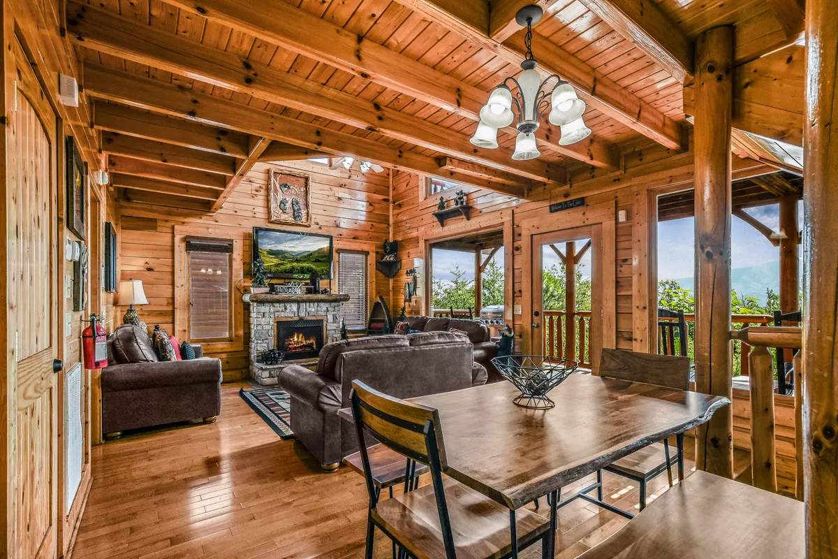 An inviting open-plan area with a fireplace, an elegant dining table set for meals, exposed wooden beams, and vast windows offering sweeping views—creating an atmosphere that is both homely and scenic, ideal for shared meals or cozy evenings.